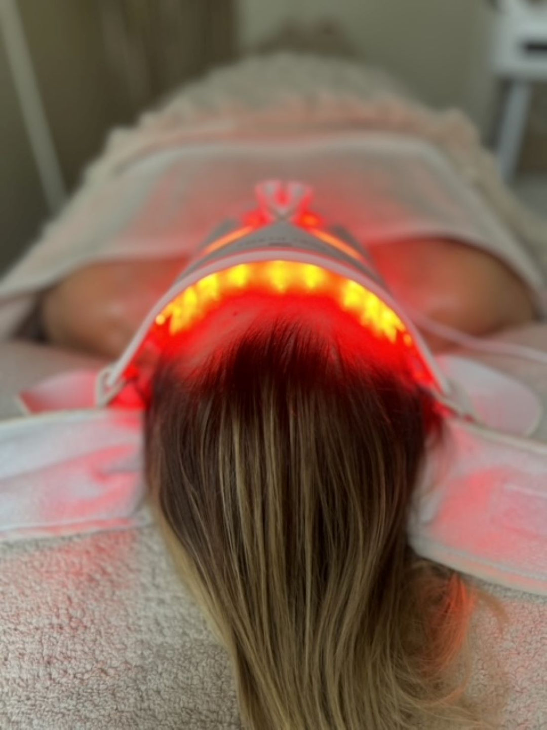 Woman lying down wearing an LED light therapy face mask during an at-home skincare session