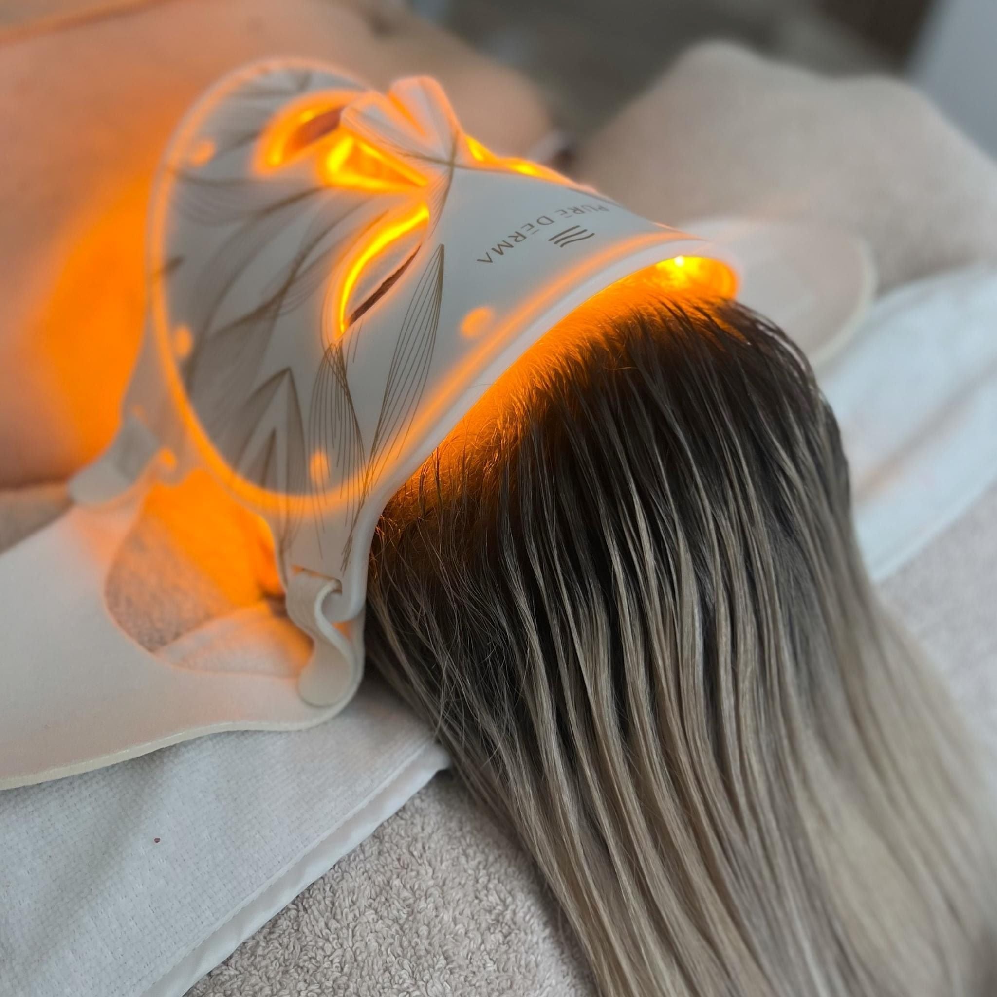 Pure Derma LED face mask glowing yellow on a client lying on a treatment bed