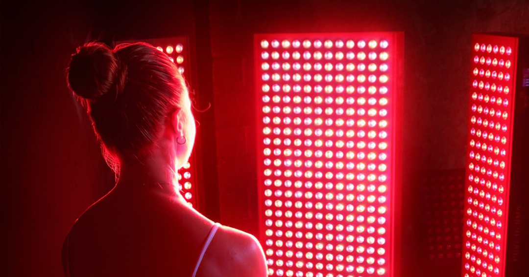 Alt text Woman standing in front of illuminated red LED light therapy panels in a dark room