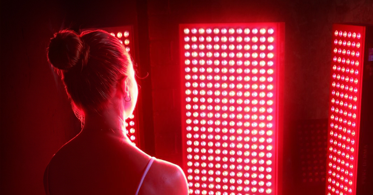 Alt text Woman standing in front of illuminated red LED light therapy panels in a dark room