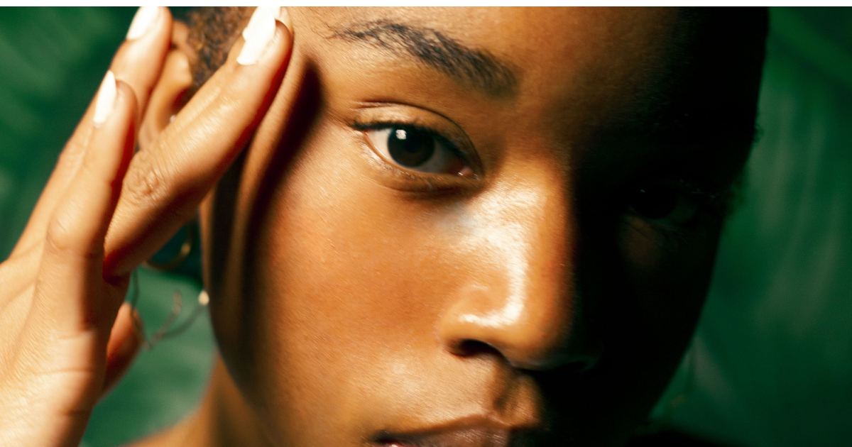 Close-up of a woman with melanin rich skin touching her face, showing smooth, radiant skin