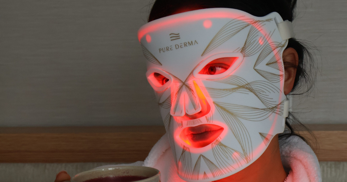 Woman sitting at home wearing a red LED light therapy face mask during her skincare routine