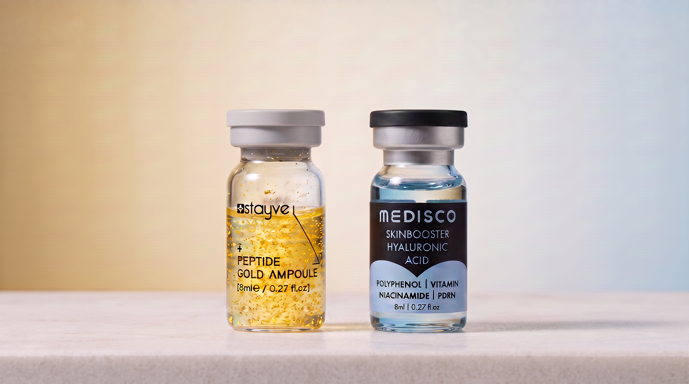 Stayve EGF Peptide Gold and Medisco Hyaluronic Acid skin booster ampoules standing side by side on a white stone surface against a soft gold to blue gradient background
