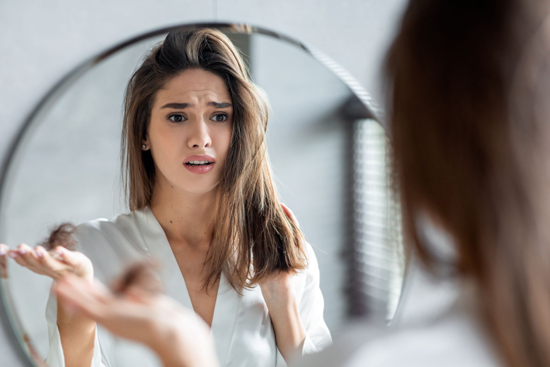 Woman looking in the mirror at her hair as part of an at-home hair care routine