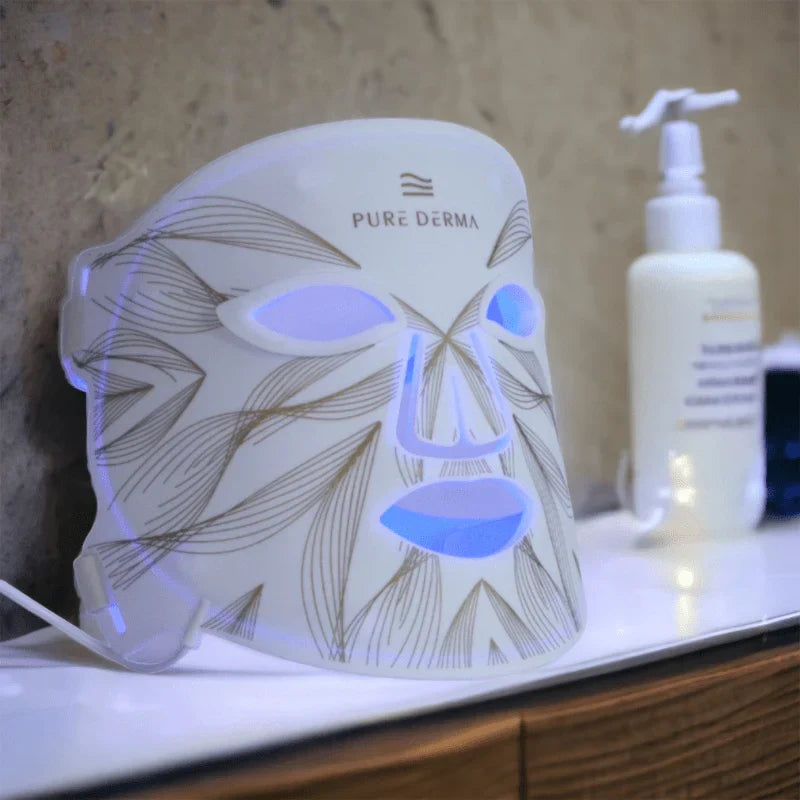 Pure Derma LED Light Therapy Face Mask lit up in blue light on a bathroom shelf at home